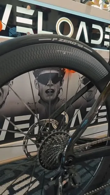 Black Cervélo S5 with deep carbon wheels in front of the Veloaded wall sign